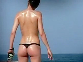 Debout une femme en string fume sur la plage